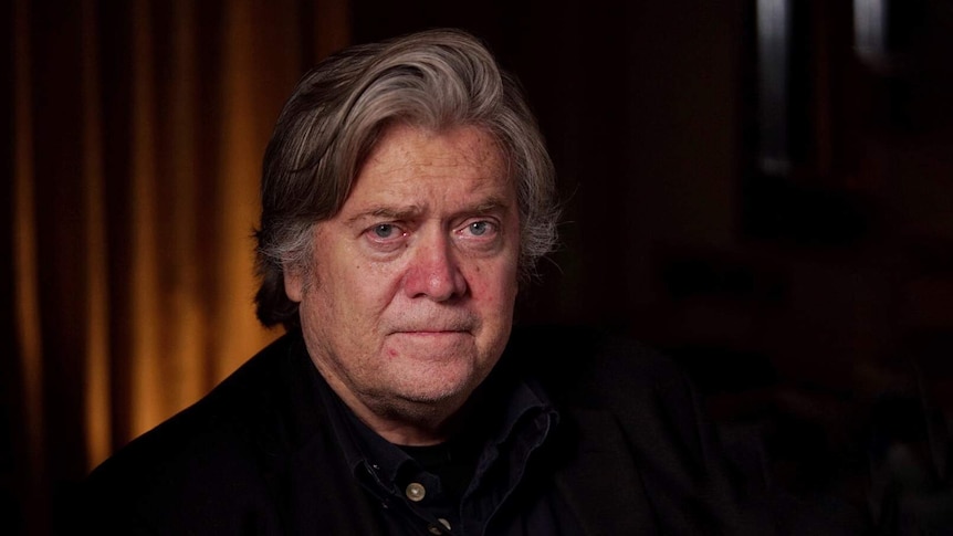 Headshot of Steve Bannon, showing him in a dark room, looking directly at the camera with a neutral expression