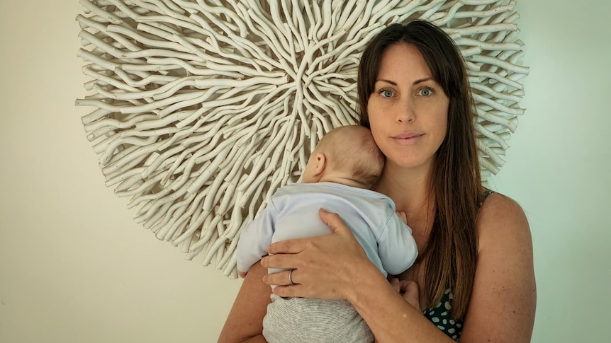 A mum with long dark hair holds a little baby against her shoulder.