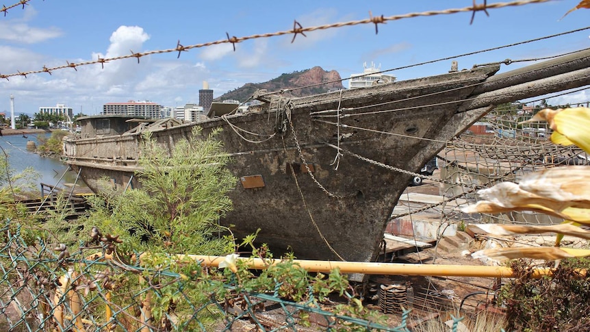 An old wooden ship covered in barnacles sits on a slipway in front of Castle Hill in Townsville
