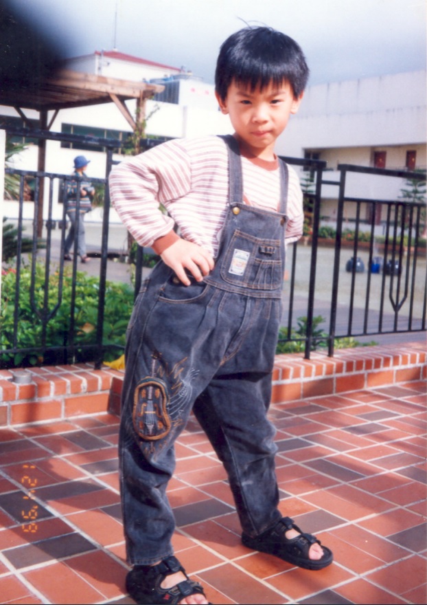 A tiny Eddy Chen wearing denim overalls with an embroidered violin, hands on hips.