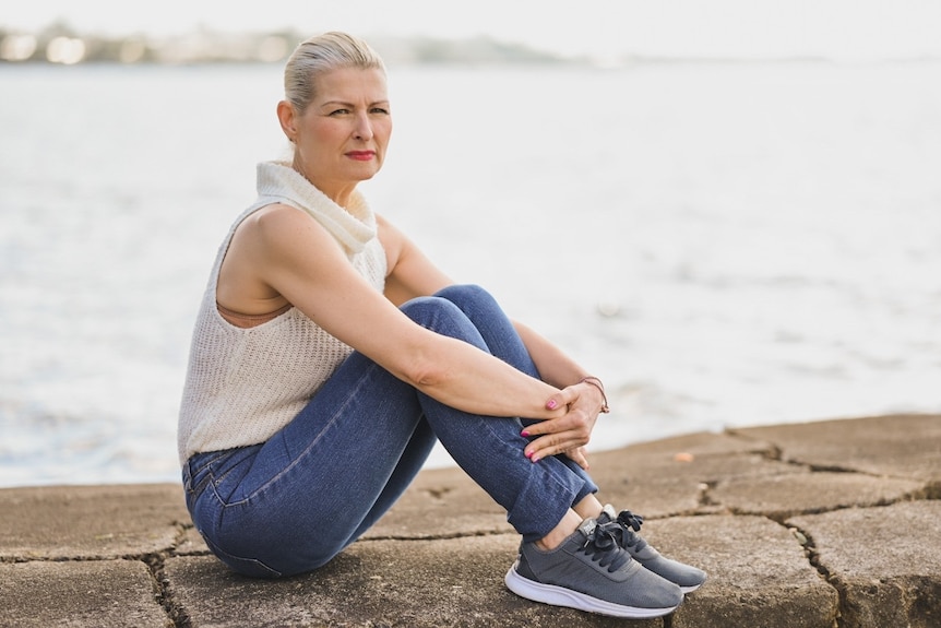 Jacqueline Goodwin sits outside at Manly with Moreton Bay behind her 