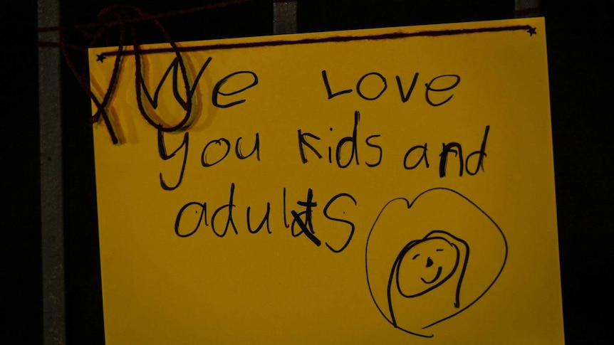 A yellow card with a child's writing saying "we love you kids and adults".