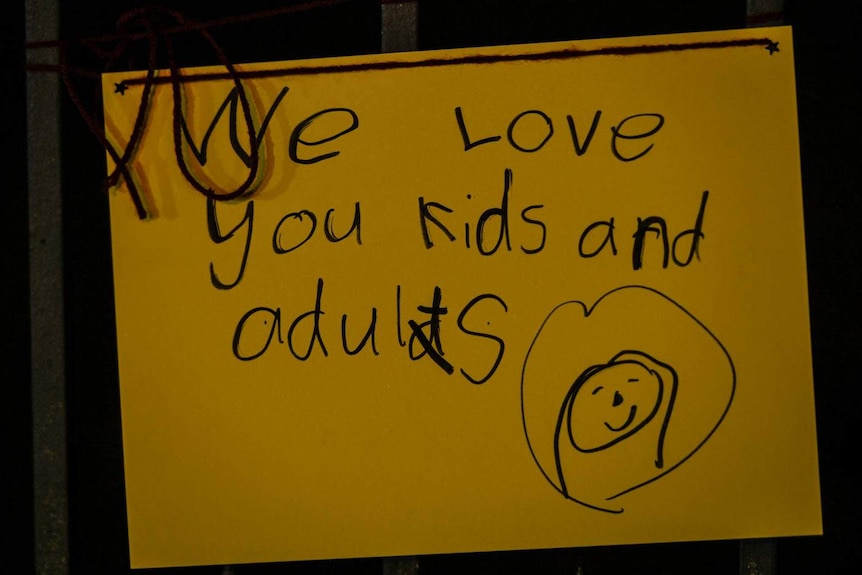 A yellow card with a child's writing saying "we love you kids and adults".
