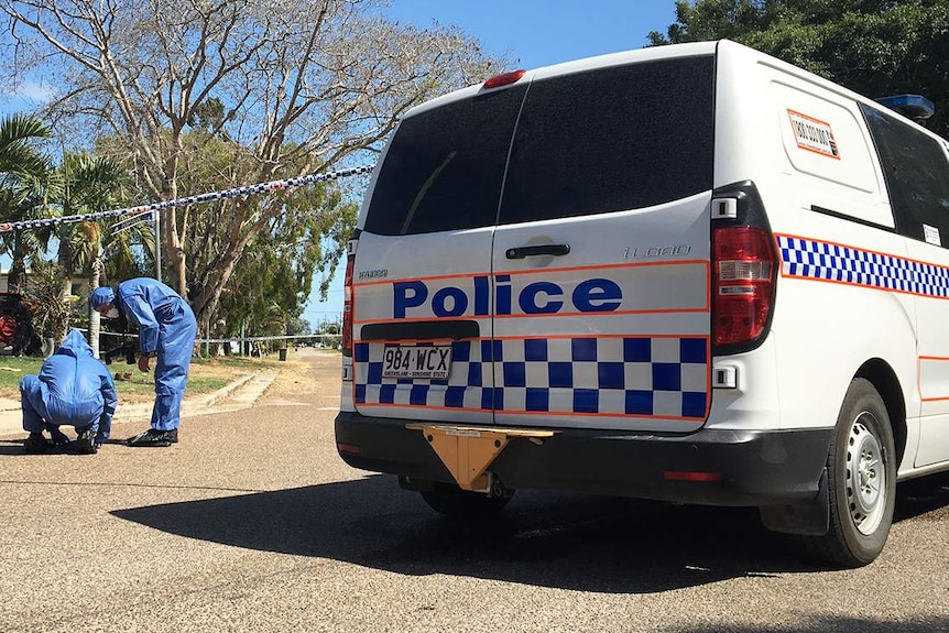 Forensic police officers kneel on road at the scene where two men died at a house at Alva Beach.