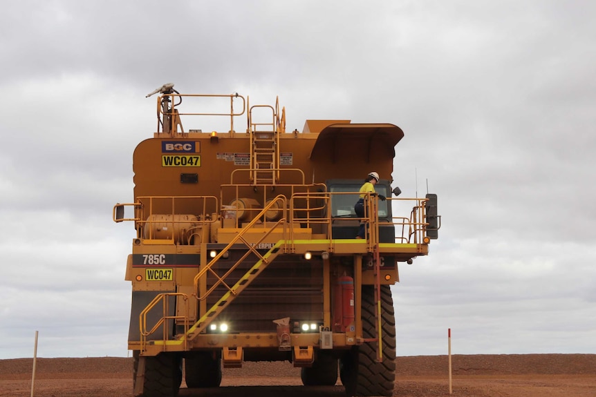 Big yellow truck parked front on, woman in high vis gear up top getting into cabin