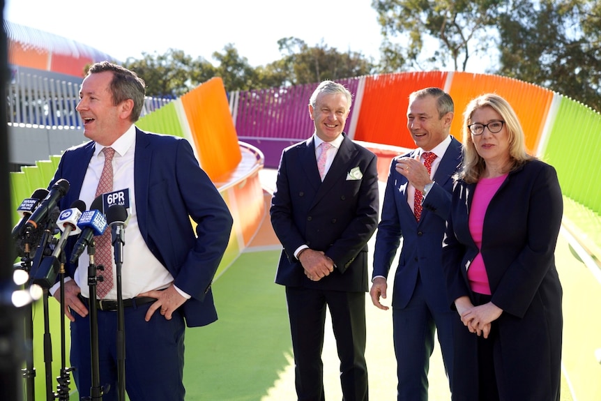 Four people in suits in front of a colourful bridge.