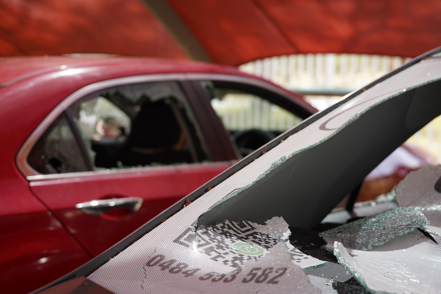 Two cars parked next to each other both have all their windows smashed