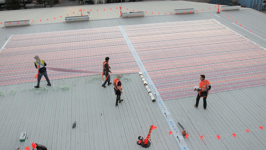 Researchers install printed solar plastic rolls on the roof of a warehouse.