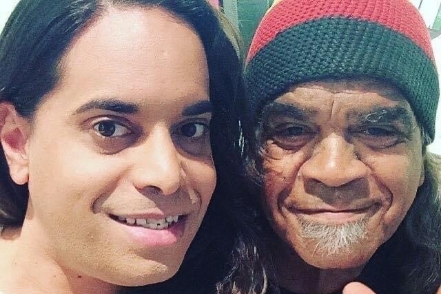 An Indigenous woman with long hair and an elderly Indigenous man wearing a beanie smile in a selfie.
