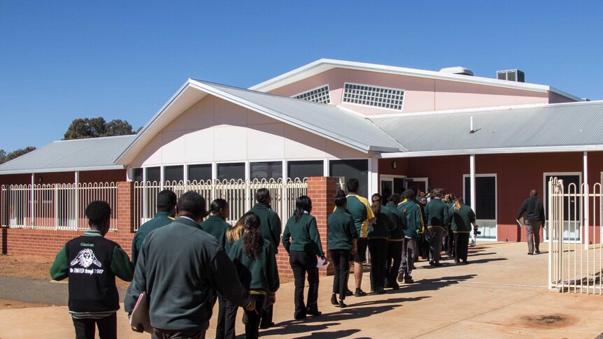 Image of a line of students walking into a school building.
