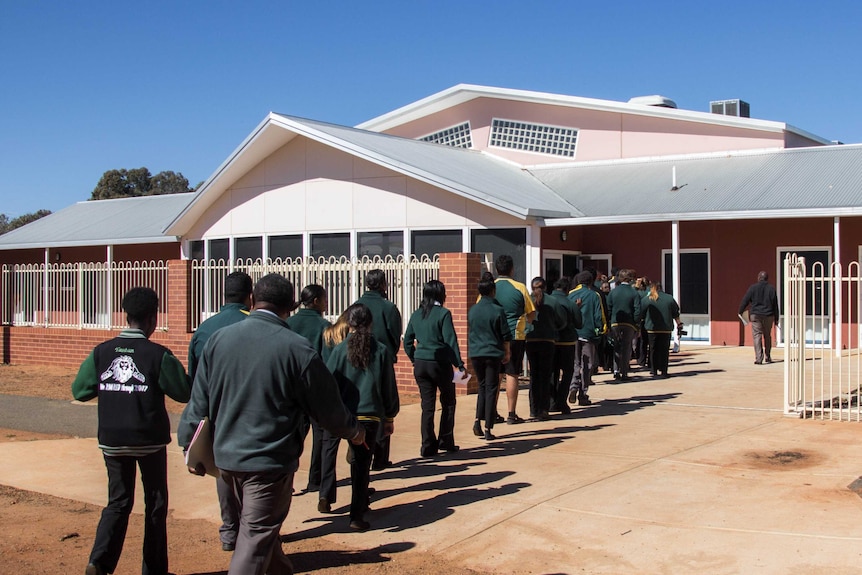 Image of a line of students walking into a school building.