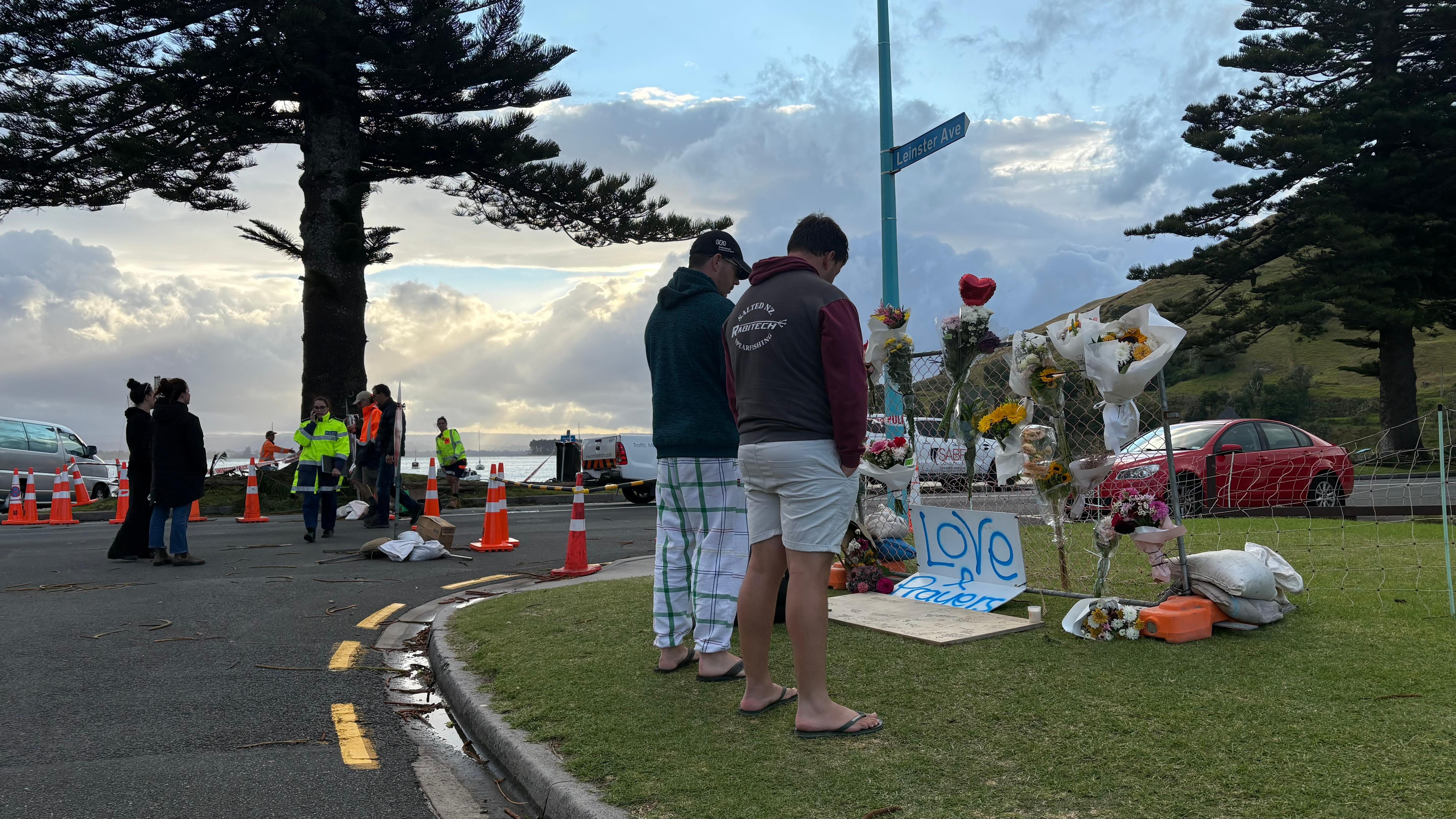Várias pessoas permanecem de cabeça baixa diante de um monumento improvisado.