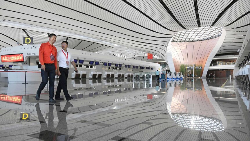 A space-age looking black and white lobby in Beijing's new airport with two workers walking.