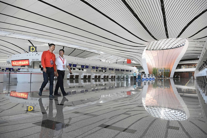 A space-age looking black and white lobby in Beijing's new airport with two workers walking.