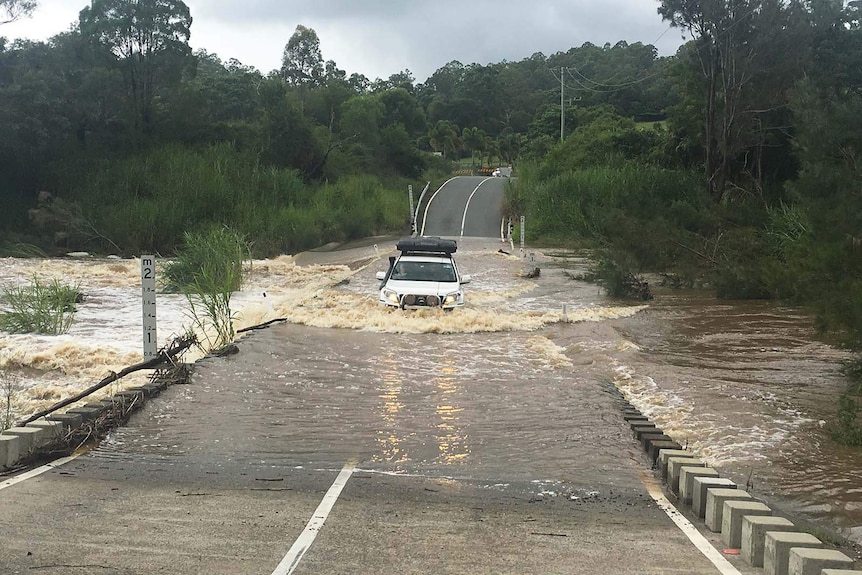 A four-wheel drive crosses a flooded causeway in the Gold Coast hinterland