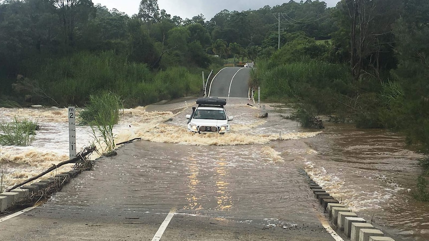 A four-wheel drive crosses a flooded causeway in the Gold Coast hinterland