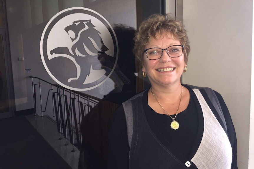 A woman stands in front of a Holden logo