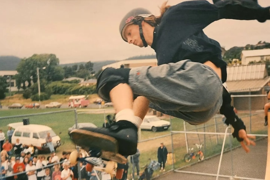 Man on skateboard wearing dark colours performs trick on skateboard.