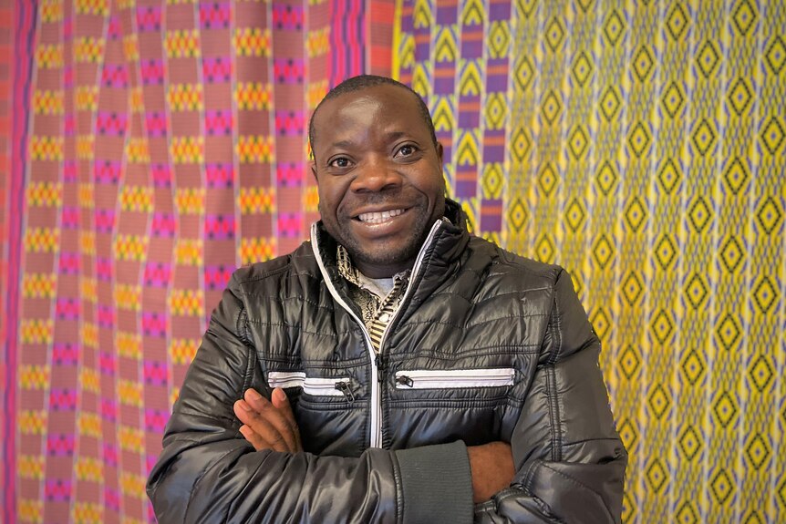 Smiling man stands in front of bright patterned fabric