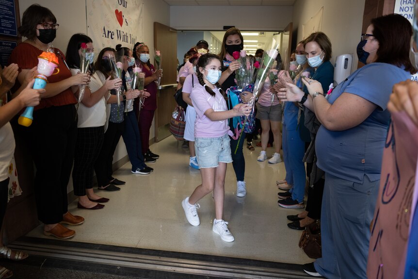 a young girl passes out roses to a crowd as she leaves hospital