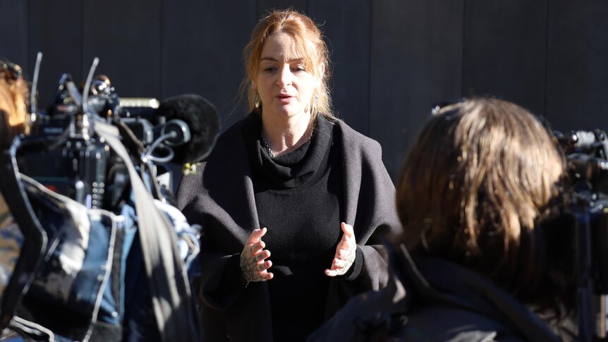 A woman gestures as she speaks to media and cameras outside a court building.