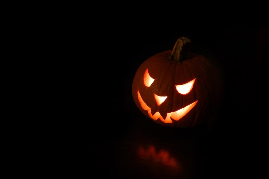 A carved pumpkin in the dark with a lit candle inside