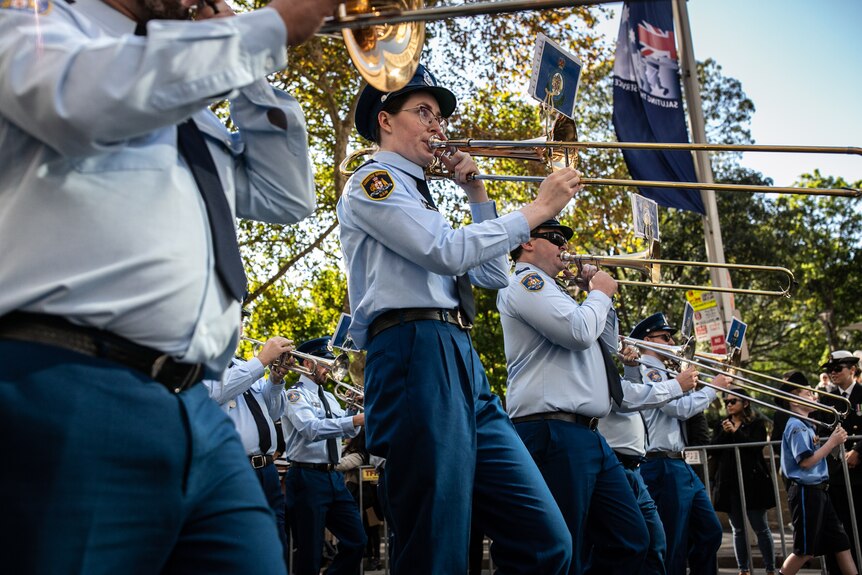A woman in uniform marches in a line while playing the trombone.