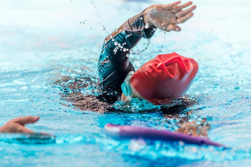 Woman doing freestyle in a pool, with the help of a kick board.