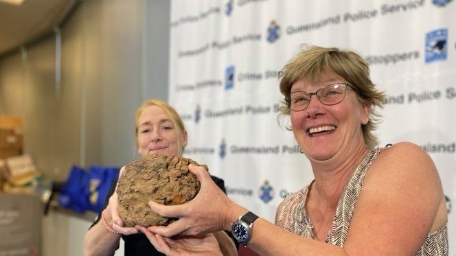 Two women hold up a soccer-ball sized meteorite sitting in front of a police banner