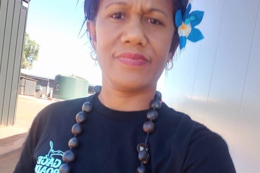 A woman wears a big necklace around her neck and a flower in her dark hair