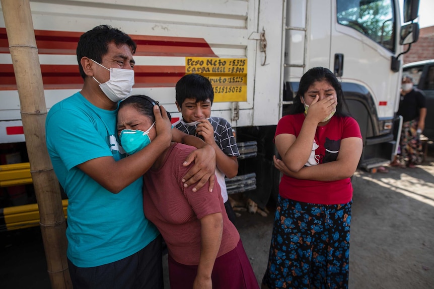 Four people cry in each others arms.