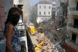 A woman stands on her balcony as she looks at rescuers searching at the site of a collapsed building in Beirut