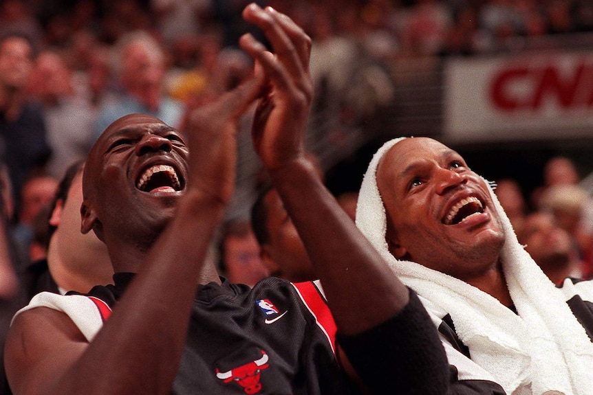Chicago Bulls teammates Michael Jordan and Ron Harper laugh and clap while on the bench during an NBA playoff game.