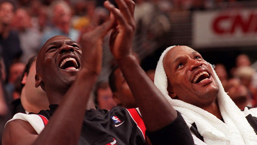 Chicago Bulls teammates Michael Jordan and Ron Harper laugh and clap while on the bench during an NBA playoff game.