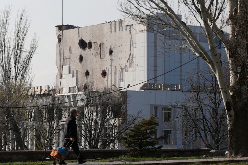 A person walks past a building that has holes in it from the fighting.