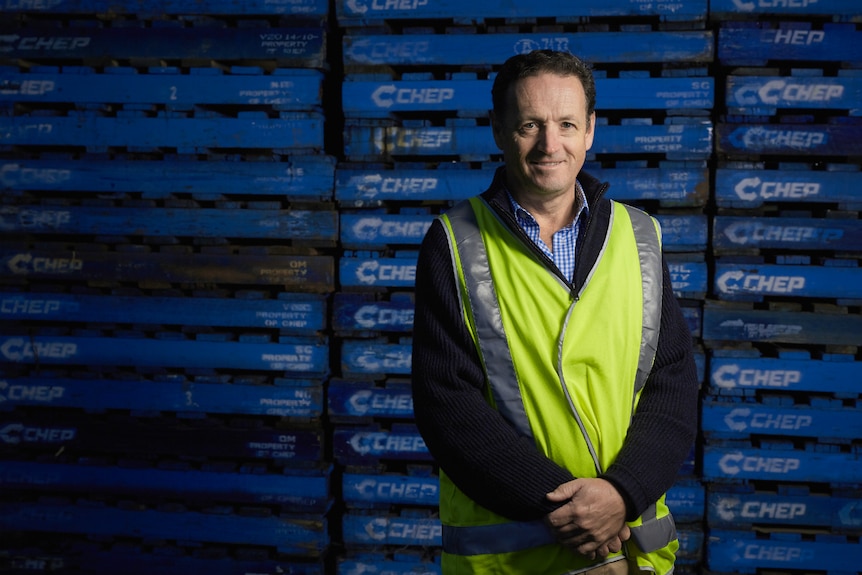 A man in a high-viz vest stands in front of towers of fruit and vegetable pallets.