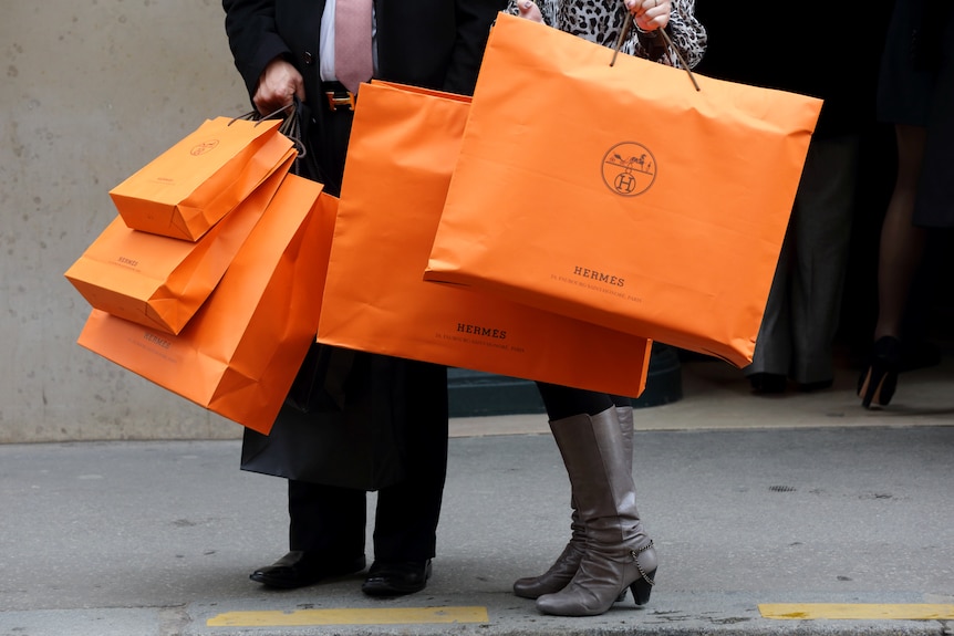 Un hombre y una mujer sosteniendo muchas bolsas de compras de color naranja.