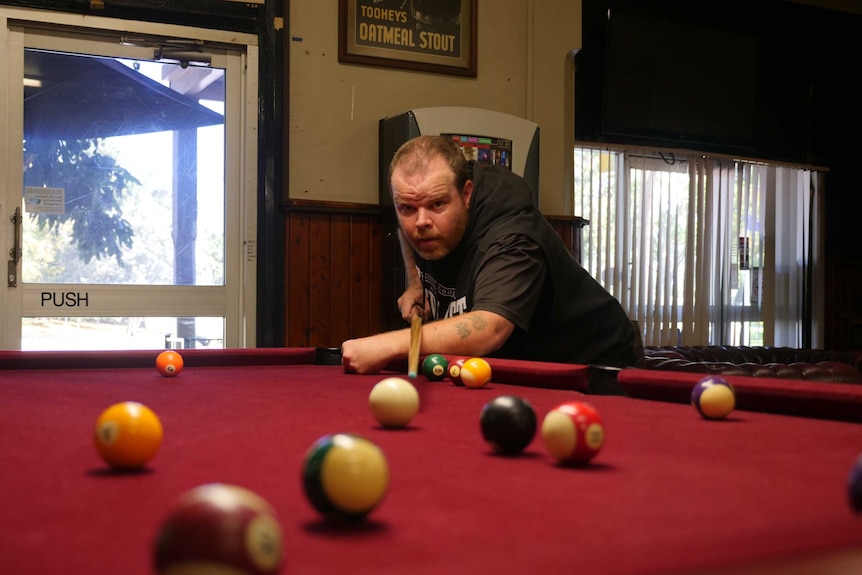 A man lines up a shot at a pool table with his right arm, using left arm folded in front of him for support
