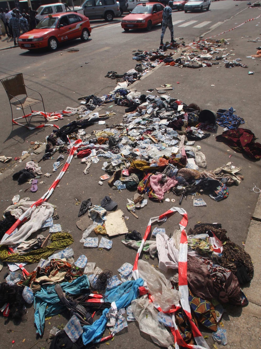 A man walks next to clothing and various items spread over the footpath following a stampede in Abidjan.