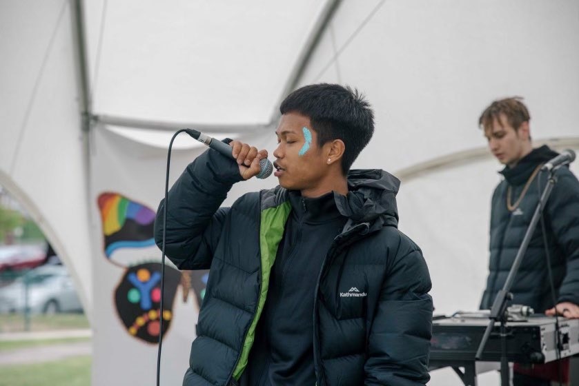 Two men wearing puffer jackets on stage, one with a microphone and one behind him producing