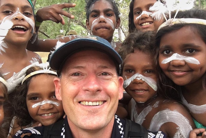 Selfie of police officer surrounded by young Aboriginal dancers in costume.