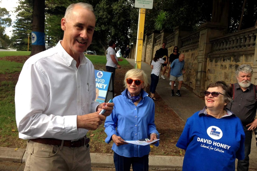 A man  stands with two elderly female Liberal supporters in blue shirts.