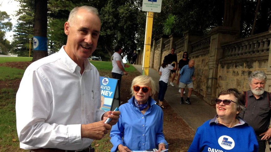 A man  stands with two elderly female Liberal supporters in blue shirts.