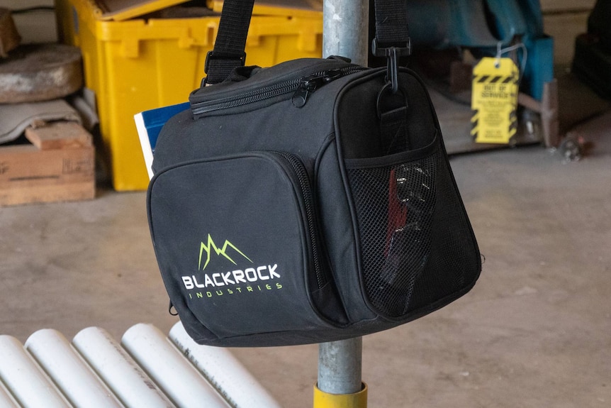 a black cooler bag, with the logo for blackrock industries, hangs on a pole in a trades workshop