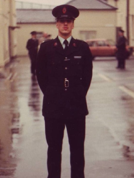 A man stands on wet ground in police uniform.