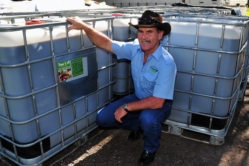 Man crouches in front of large agricultural tubs of biological fertiliser.