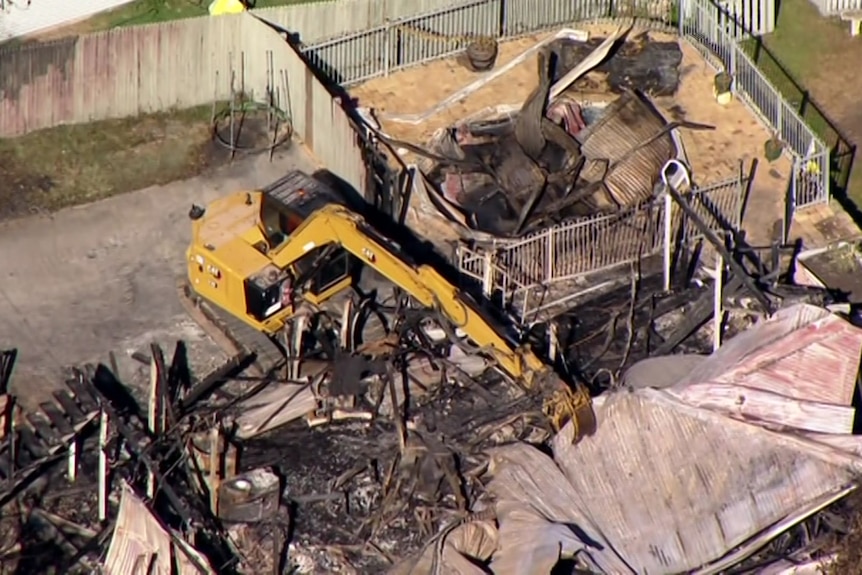 Heavy machinery removing the roof of a burnt house.