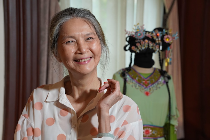 Gabrielle Chan smiles, posing with no make up on, in front of a Chinese opera costume on a mannequin