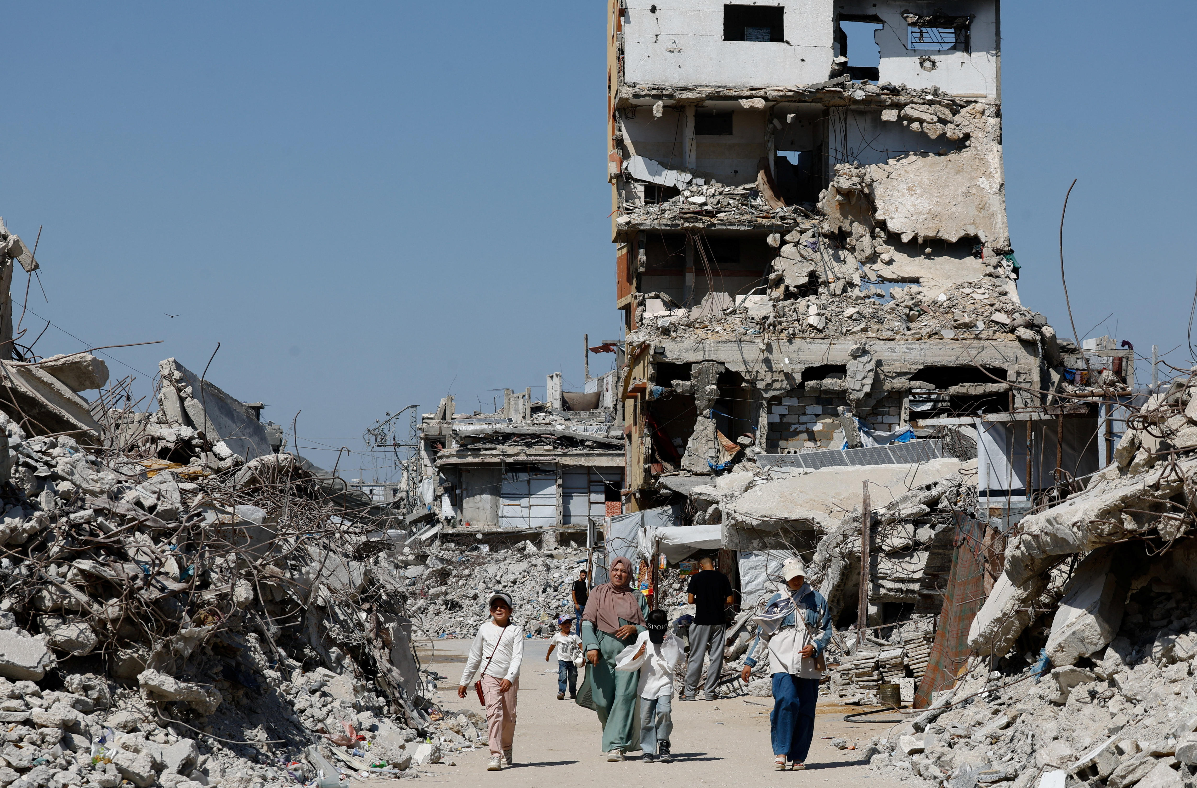 A group of people walking down a road with piles of rubble and a partially destroyed apartment building around them.
