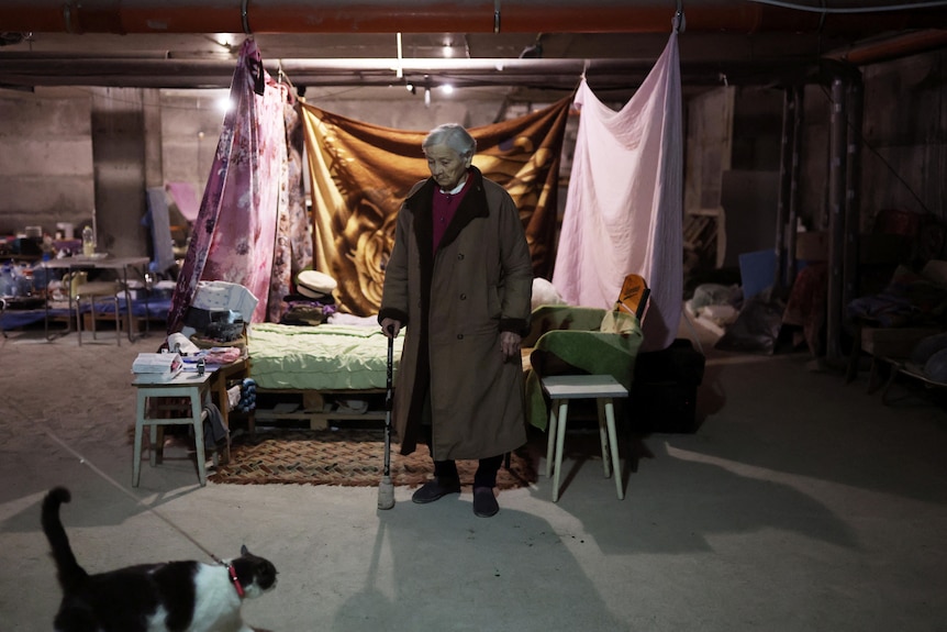 Maria Nikolaevna, 92, looks at her family cat, Kisiau, next to her makeshift basement bedroom